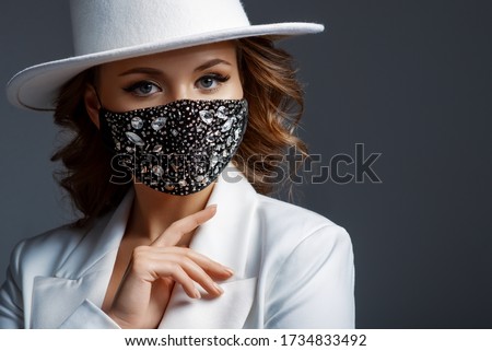Elegant woman wearing trendy fashion outfit during quarantine of coronavirus outbreak. White suit including stylish luxury black face mask with rhinestones. Close up studio portrait. Copy, empty space