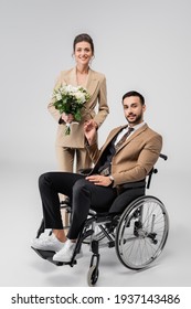 elegant woman with wedding bouquet, and handicapped muslim man looking at camera on grey