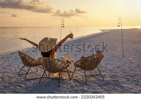 A elegant woman in a white dress enjoys the tropical sunset with a cocktail on a beach in the Maldives islands