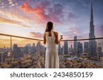 A elegant woman in a white evening dress enjoys the beautiful sunset view behind the modern skyline of Downtown Dubai, UAE