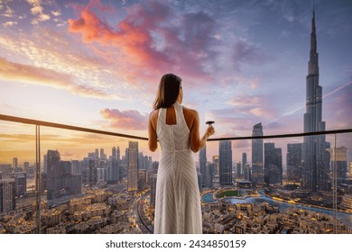 A elegant woman in a white evening dress enjoys the beautiful sunset view behind the modern skyline of Downtown Dubai, UAE - Powered by Shutterstock
