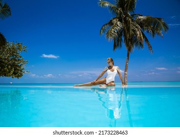 Elegant woman in white swimsuit in pool on tropical Maldives island. Beautiful bikini body girl in pool with view on horizon. Elegant model near the pool on beautiful Indian ocean landscape. Travel