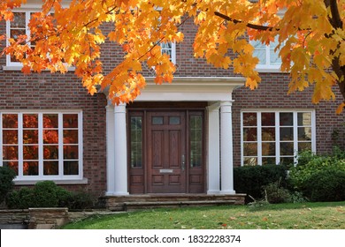 Elegant Wooden Front Door Of Traditional Two Story Brick House With Maple Tree In Brilliant Fall Color