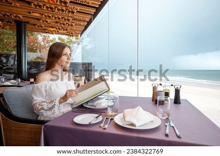 Elegant young adult at beachfront restaurant, casual attire, contemplating ocean view, luxury dining ambiance, travel dining experience.