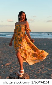 An Elegant Young Caucasian Female Model Posing At The Beach In A Beautiful Yellow Dress With Floral Patterns