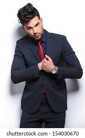 Elegant Young Fashion Man In Tuxedo Searching In His Chest Pocket While Looking At The Camera. On Gray Background