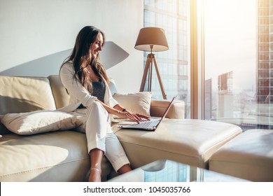 Elegant young female business woman using a laptop sitting on a sofa at home