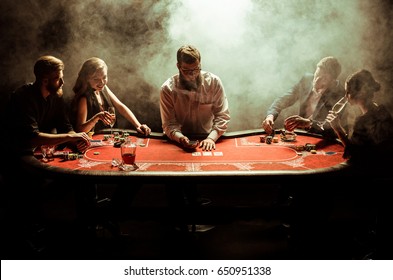 Elegant Young Men And Women Playing Poker At Table In Smoke