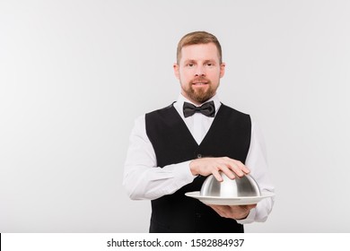 Elegant Young Waiter In Bowtie And Black Waistcoat Holding Cloche With Food For One Of Clients Of Restaurant