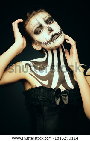 Elegant young woman in black top with pumpkin skull make-up over black background. Pumpkin queen. Costumes and makeup for Halloween. Copy space.