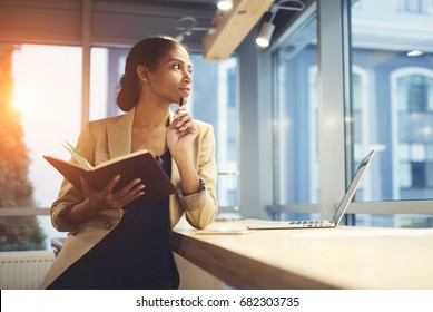 Elegant young woman looking away thoughtfully while holding notepad and leaning on table with laptop. Successful Afro American female pondering about business strategy for enterprise - Powered by Shutterstock