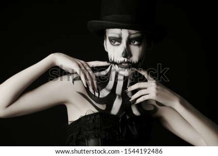 Elegant young woman in a male top-hat with pumpkin skull make-up over black background. Pumpkin queen. Costumes and makeup for Halloween. Copy space.
