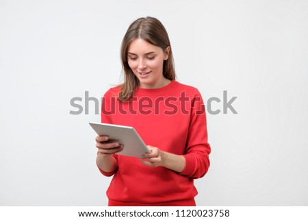 Elegant young woman in red sweater using tablet, looking at screen. Use modern technologies in common everyday life