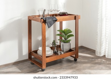 An elegantly crafted wooden serving trolley featuring a variety of stemmed glasses and a potted plant
