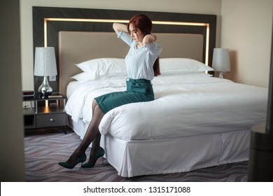 Elegantly Dressed Business Woman In Green Pencil Skirt And Stilettos, Relaxing On Hotel Room Bed After A Long Business Trip.