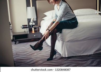 Elegantly Dressed Business Woman, Relaxing On Hotel Room Bed After A Long Business Trip. Red-haired Lady Rubbing Legs And Takes Off Her Stilettos