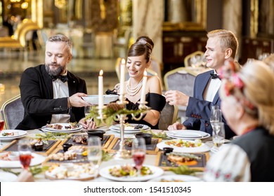 Elegantly dressed group of people having a festive dinner at a well-served table with tasty dishes during New Year Eve at the luxury restaurant - Shutterstock ID 1541510345