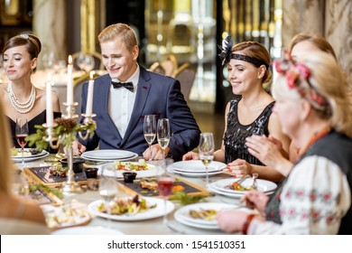 Elegantly dressed group of people having a festive dinner at a well-served table with tasty dishes during New Year Eve at the luxury restaurant - Shutterstock ID 1541510351