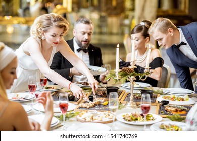 Elegantly dressed group of people having a festive dinner at a well-served table with tasty dishes during New Year Eve at the luxury restaurant - Shutterstock ID 1541740769