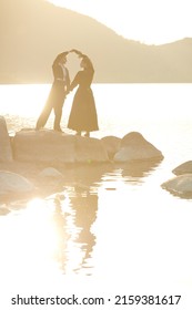 Elegantly Dressed Loving Couple Stand By The Sea At Sunset Holding Their Hands And Looking At Each Other's Eyes. Historical Romance Novel. Loving  Relationship. 19th Century Style.