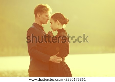 Elegantly dressed loving couple stand close to each other by the sea at sunset tenderly looking at each other. Historical romance novel. Loving  relationship. 19th century style.