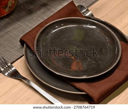 Elegantly set dining table with dark ceramic plates and rich brown napkins, ready for a meal.
