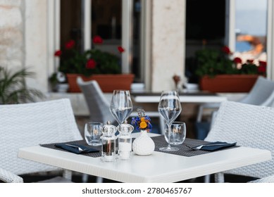 An elegantly set empty dining table waits for guests at a charming outdoor restaurant terrace in Europe. Mediterranean dining and romantic summer vacation concept.