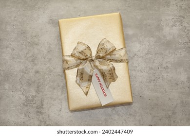 An elegantly wrapped gift in gold tones with a Happy Holidays gift tag. - Powered by Shutterstock