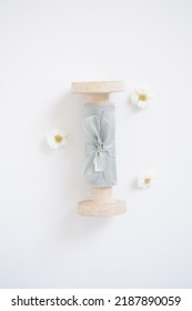 An Element For A Wedding, A Light Blue Silk Ribbon On A Wooden Role Lies On A White Background Next To Small Daisies
