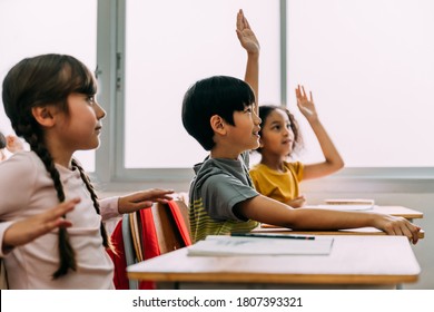 Elementary age Asian student boy raised hands up in Q and A class. Diverse group of pre-school pupils in elementary age in education building school. Volunteering and participating classroom concept. - Powered by Shutterstock