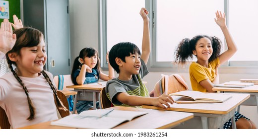 Elementary age Asian student boy raised hands up in class. Diverse group of pre-school pupils in elementary age in education building school. Volunteering and participating classroom concept. - Shutterstock ID 1983261254