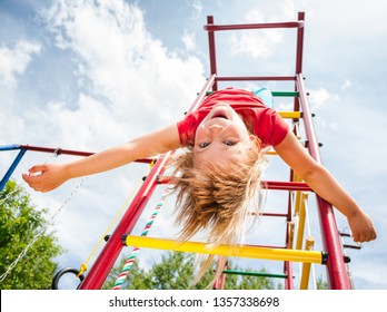 Elementary age girl hanging upside down from a jungle gym (monkey bars or climbing frame) in a playground enjoying summertime