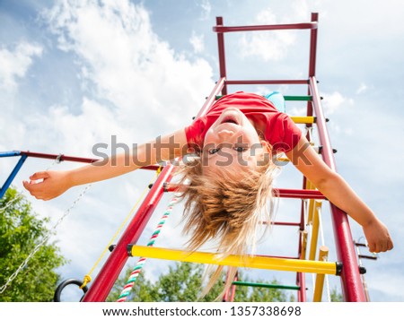 Elementary age girl hanging upside down from a jungle gym (monkey bars or climbing frame) in a playground enjoying summertime