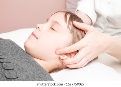 Elementary Age Girl Receiving Osteopathic Or Chiropractic Treatment In Pediatric Clinic. Manual Therapist Manipulates Child's Scull