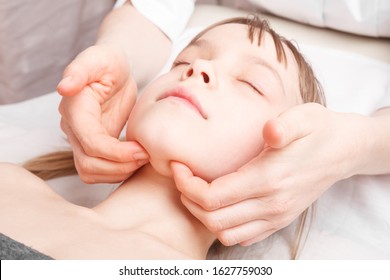 Elementary Age Girl Receiving Osteopathic Or Chiropractic Treatment In Pediatric Clinic. Manual Therapist Manipulates Child's Jaw