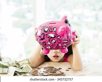 Elementary Aged Child With Piggy Bank Money Spread Out On Table