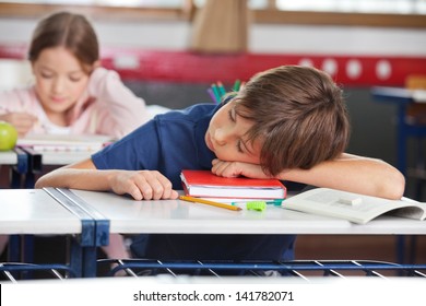 Elementary boy sleeping while girl studying in background at classroom - Powered by Shutterstock