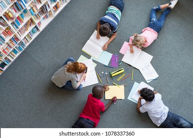 Elementary children lying the floor   drawing at library  Top view five multiethnic boys   girls in daycare house drawing copybook  High angle view group kids and colorful pencils 