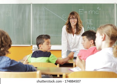 Elementary classroom. Focus on teacher standing in front of chalkboard.