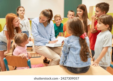 Elementary female teacher talking with schoolkids sitting on bench in classroom - Powered by Shutterstock