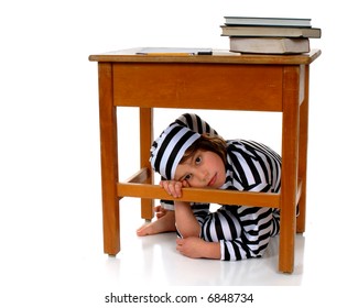 An Elementary Girl In Striped Prison Garb Hiding Under Her School Desk.