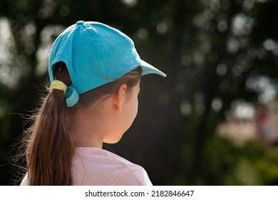 Elementary School Age Child, Girl Looking At Something, Seen From Behind, Copy Space, Back Of The Head Closeup Baseball Cap Blurred Background, One Person Outdoors Portrait, Watching Something Concept