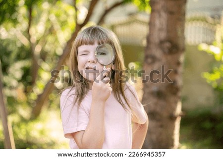 Elementary school age child looking through a large magnifying glass holding it next to one eye funny portrait, smart intelligent kid explorer Closer look, magnification, science research, exploration
