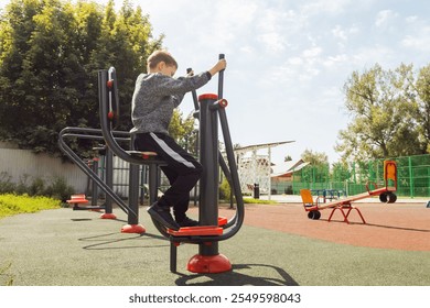 Elementary school boy using stepper machine at outdoor fitness playground. Health, children's fitness, public recreational facilities, and active lifestyle promotional content.