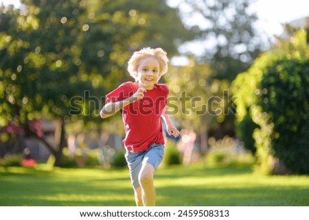 Elementary school child running on lawn in urban park on sunny day. Happy preteen boy having fun during walk. Outdoors activity for children on summer holidays