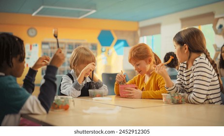 Elementary School Children Eating Healthy Food on a Lunch Break. Smart Diverse Kids Having Fun, Talking and Enjoying Tasty Salad Meals in a Modern Colorful Classroom Between Educational Lessons - Powered by Shutterstock