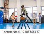Elementary school children practicing gymnastics, a boy jumping over a pommel horse in a school gym