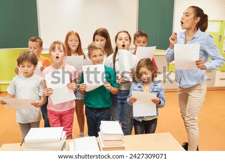 Elementary school children singing choir with female teacher standing in classroom