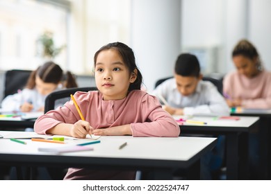 Elementary School Class. Portrait of Cute Little Asian Girl Smiling, Taking Notes And Writing in Exercise Notebook. Junior Classroom with Diverse Group of Children Learning New Stuff - Powered by Shutterstock