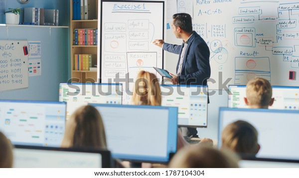 Elementary School Class: Teacher Uses\
Interactive Digital Whiteboard, Explains Lesson to Diverse Group of\
Smart Children. Kids getting Modern Education, Learn Computer\
Science, Software\
Programming